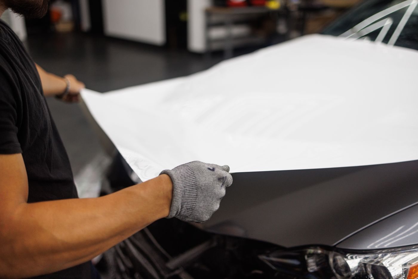 **Laying in.** A full sheet goes over the hood in one piece. Handles, badges and lights come off first so the edges tuck under instead of sitting on top of the panel.